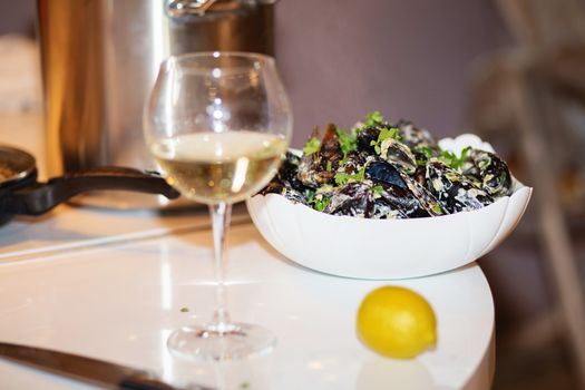 Steamed mussels in cheese sauce. Mussels in shells in the bowl with white wine on the table.