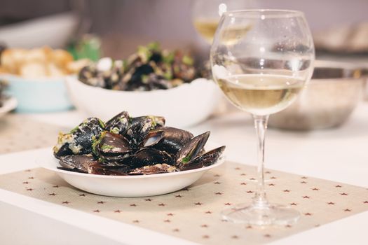 Steamed mussels in cheese sauce. Mussels in shells in the bowl with white wine on the table.