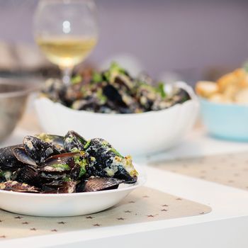 Steamed mussels in cheese sauce. Mussels in shells in the bowl with white wine on the table.