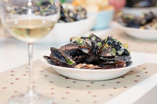 Steamed mussels in cheese sauce. Mussels in shells in the bowl with white wine on the table.