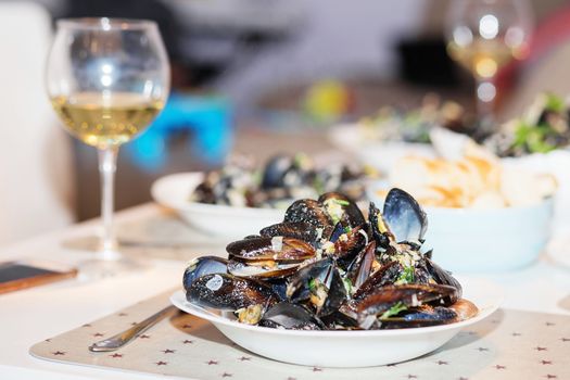 Steamed mussels in cheese sauce. Mussels in shells in the bowl with white wine on the table.