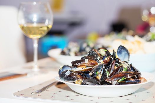 Steamed mussels in cheese sauce. Mussels in shells in the bowl with white wine on the table.