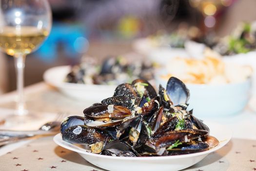 Steamed mussels in cheese sauce. Mussels in shells in the bowl with white wine on the table.