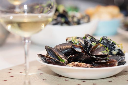 Steamed mussels in cheese sauce. Mussels in shells in the bowl with white wine on the table.