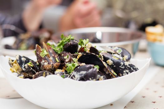 Steamed mussels in cheese sauce. Mussels in shells in the bowl with white wine on the table.