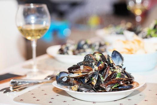 Steamed mussels in cheese sauce. Mussels in shells in the bowl with white wine on the table.