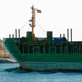 Green cargo ship's bow against lighthouse in still water, Riga