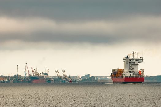 Red cargo container ship entering the port of Riga in cloudy day
