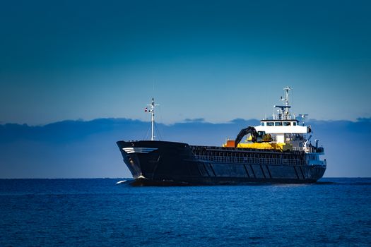 Black cargo ship with long reach excavator moving by baltic sea