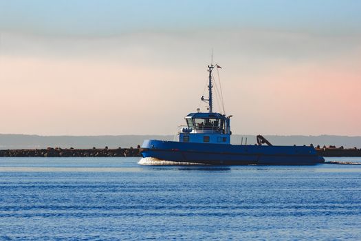Blue small tug ship sailing past the breakwater dam in morning