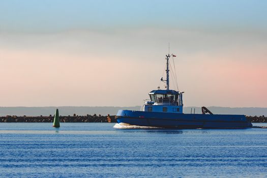 Blue small tug ship sailing past the breakwater dam in morning