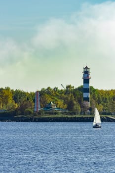 Small sailboat traveling past the lighthouse in sunny day