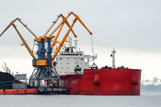 Large red cargo ship loading with a coal in the port