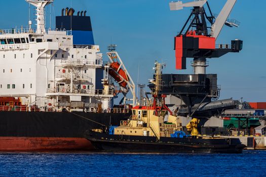 Black cargo ship mooring at the port with tug ship support