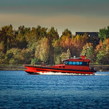 Red pilot ship moving past the autumn trees in Europe