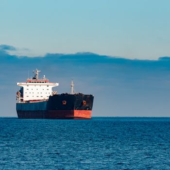 Black cargo ship moving in still Baltic sea water. Riga, Europe