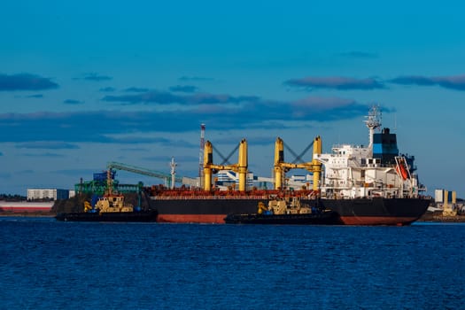 Black cargo ship mooring at the port with tug ship support