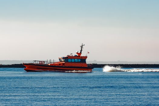 Red pilot ship moving at speed past the breakwater dam