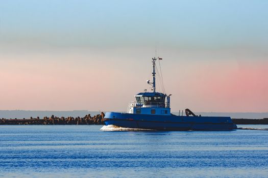 Blue small tug ship sailing past the breakwater dam in morning