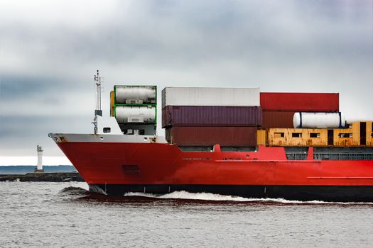 Red cargo container ship's bow in cloudy day