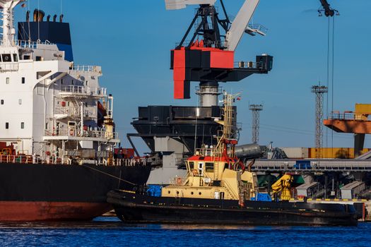 Black cargo ship mooring at the port with tug ship support