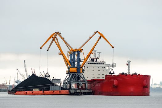 Large red cargo ship loading with a coal in the port