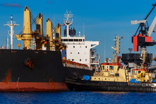 Black cargo ship mooring at the port with tug ship support