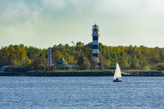 Small sailboat traveling past the lighthouse in sunny day