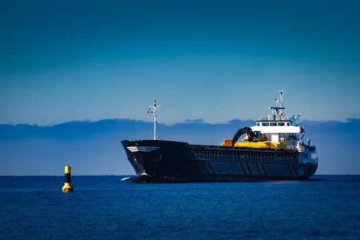 Black cargo ship with long reach excavator moving by baltic sea