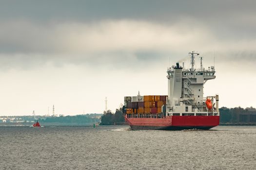 Red cargo container ship entering the port of Riga in cloudy day