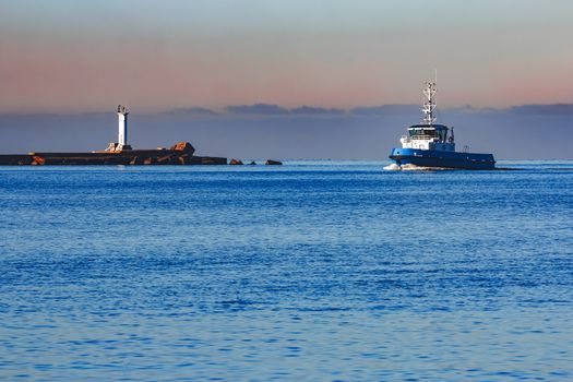 Blue small tug ship sailing past the breakwater dam in morning