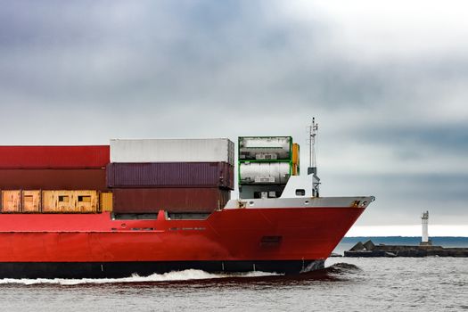 Red cargo container ship's bow in cloudy day