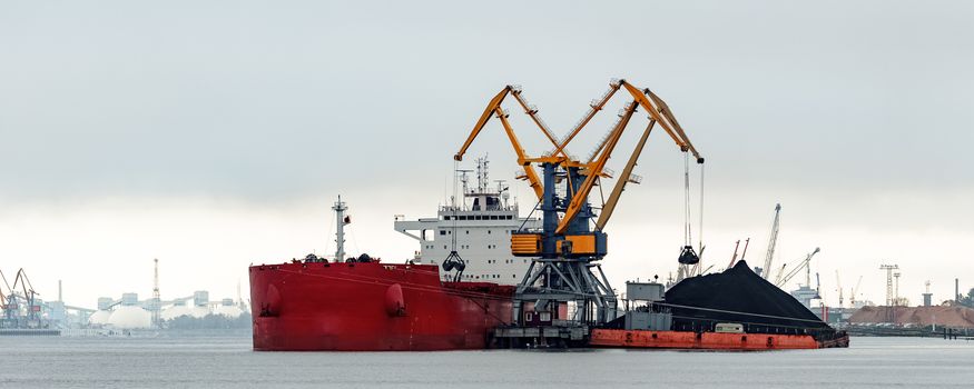 Large red cargo ship loading with a coal in the port