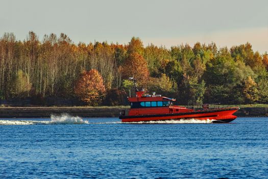 Red pilot ship moving past the autumn trees in Europe