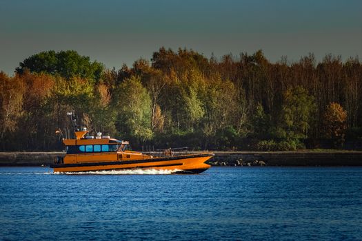 Orange pilot ship sailing past the autumn trees in Europe