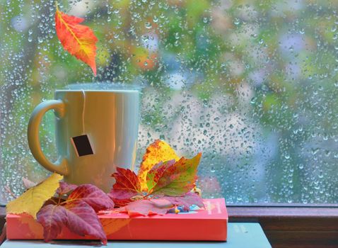 Tea cup at the window with  leaves and drops after rain in autumn 