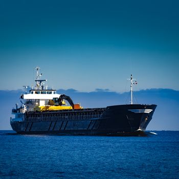 Black cargo ship with long reach excavator moving by baltic sea