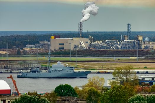 Military ship sailing past the cargo port in Riga, Latvia