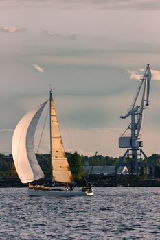 Sailboat moving past the cargo crane in evening, Latvia