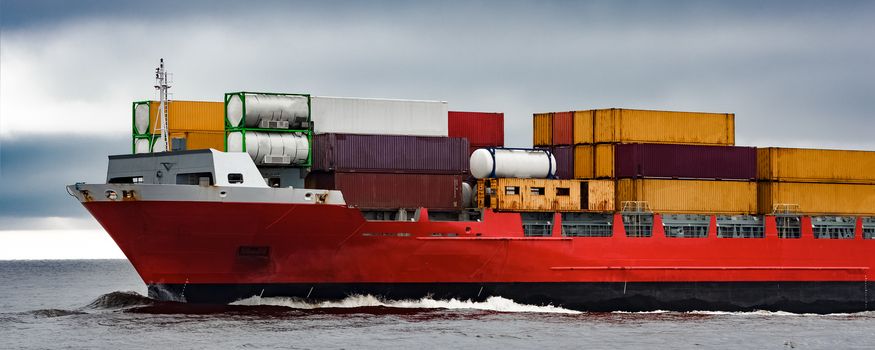 Red cargo container ship's bow in cloudy day