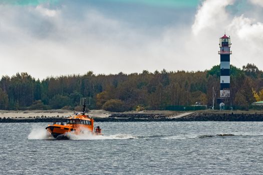 Orange pilot ship moving at speed past the lighthouse in Riga