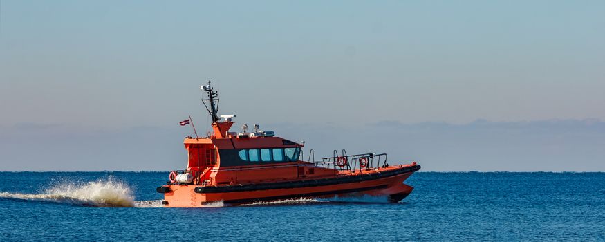 Red pilot ship moving at speed past the breakwater dam