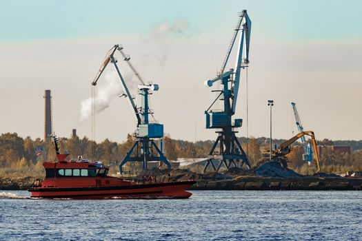 Orange pilot ship sailing against the cargo cranes