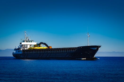 Black cargo ship with long reach excavator moving by baltic sea