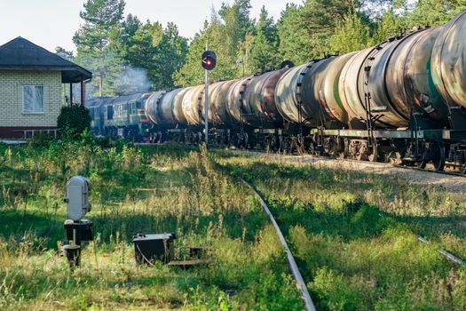 Freight train with tank wagons in forest. Green cargo locomotive