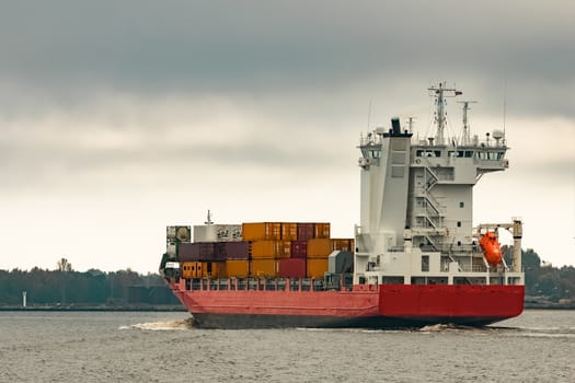 Red cargo container ship entering the port of Riga in cloudy day