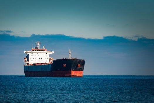 Black cargo ship moving in still Baltic sea water. Riga, Europe