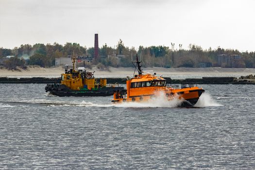 Orange pilot ship moving at speed past the tug ship in Riga