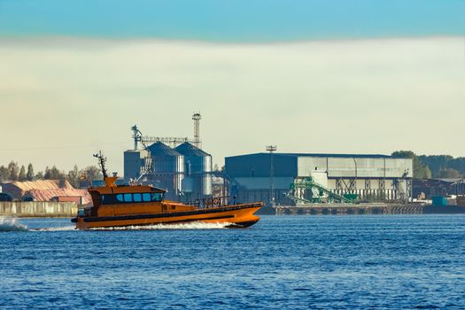 Orange pilot ship sailing past the factory in Latvia