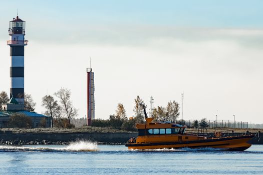 Orange pilot ship sailing past the lighthouse in Riga